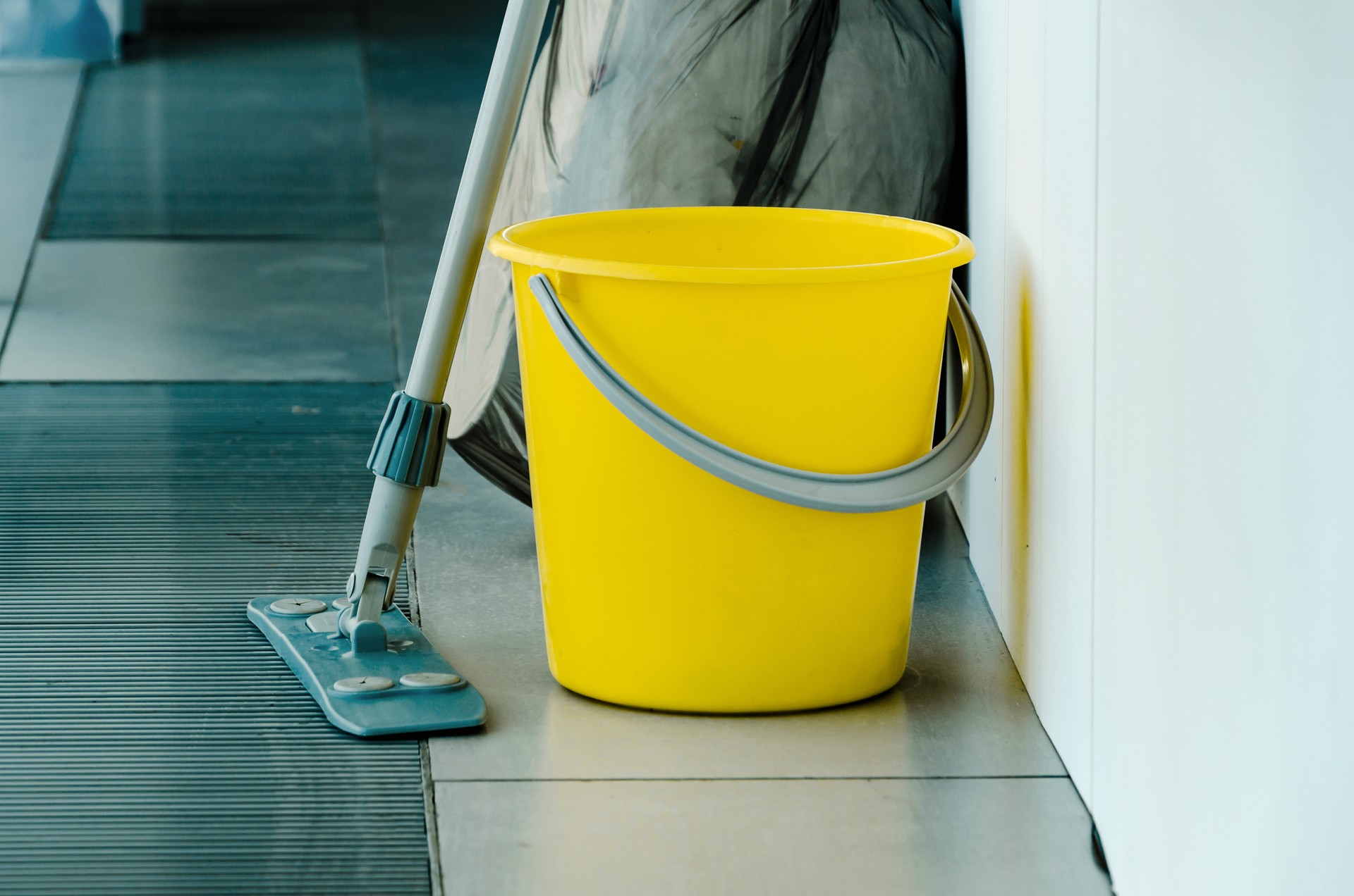 There is yellow bucket and mop on floor, tools for cleaning premises